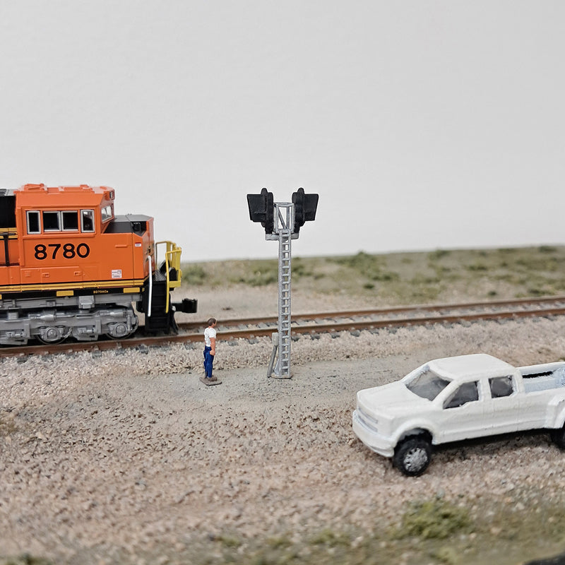 Model train set with orange locomotive, white truck, and person near a signal light on a track.