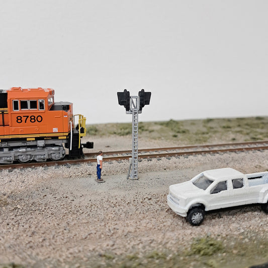 Model train set with orange locomotive, white truck, and person near a signal light on a track.