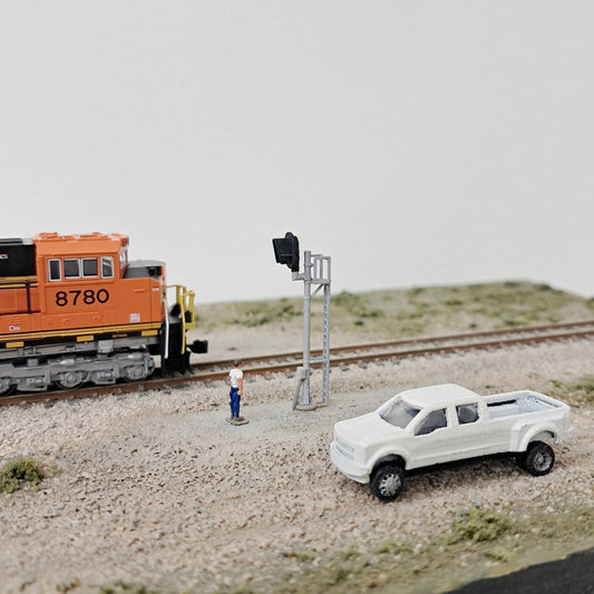 Model train set with a locomotive, truck, and railroad signal next to a track.